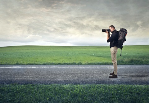 Man standing on a road with a field of grass in the background taking a picture
