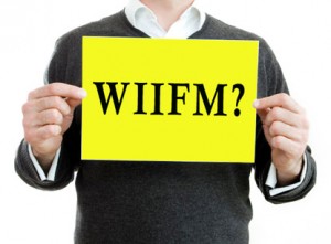 Image of man holding a card that has WIIFM? written on it.