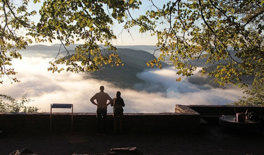 A couple looking out at an impressive mountain range, all blanketed in clouds. 