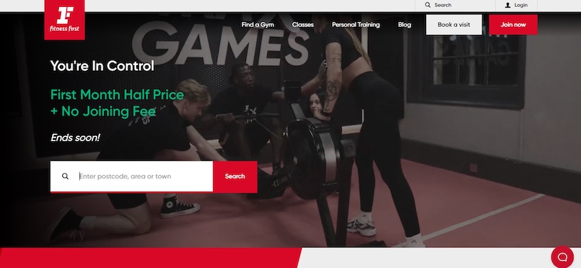 Pagina de pornire Fitness First cu o imagine a patru persoane într-o sală de sport și o bară de căutare pentru a găsi o sală de sport locală. 